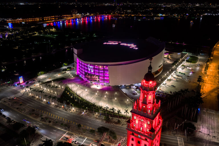 Aerial view at night of the red-lit Freedom Tower and the arena glowing pink with Vice City signage, downtown Miami, by Arte City Media