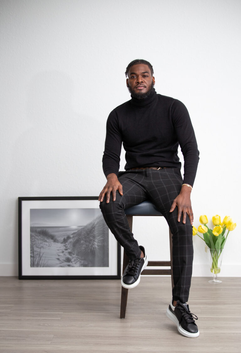 Studio portrait of a man in a black turtleneck seated on a stool